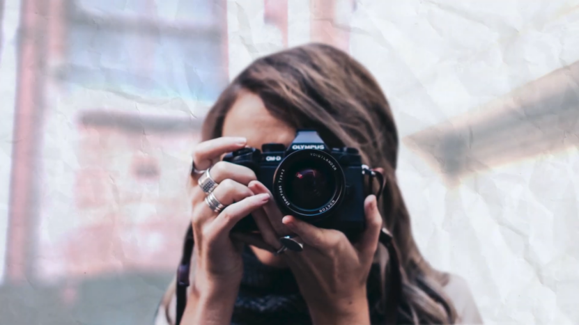 A Person Holding a Camera up To Their Face, Capturing a Photo, with A Textured, Crumpled Paper Effect Overlaying the Image