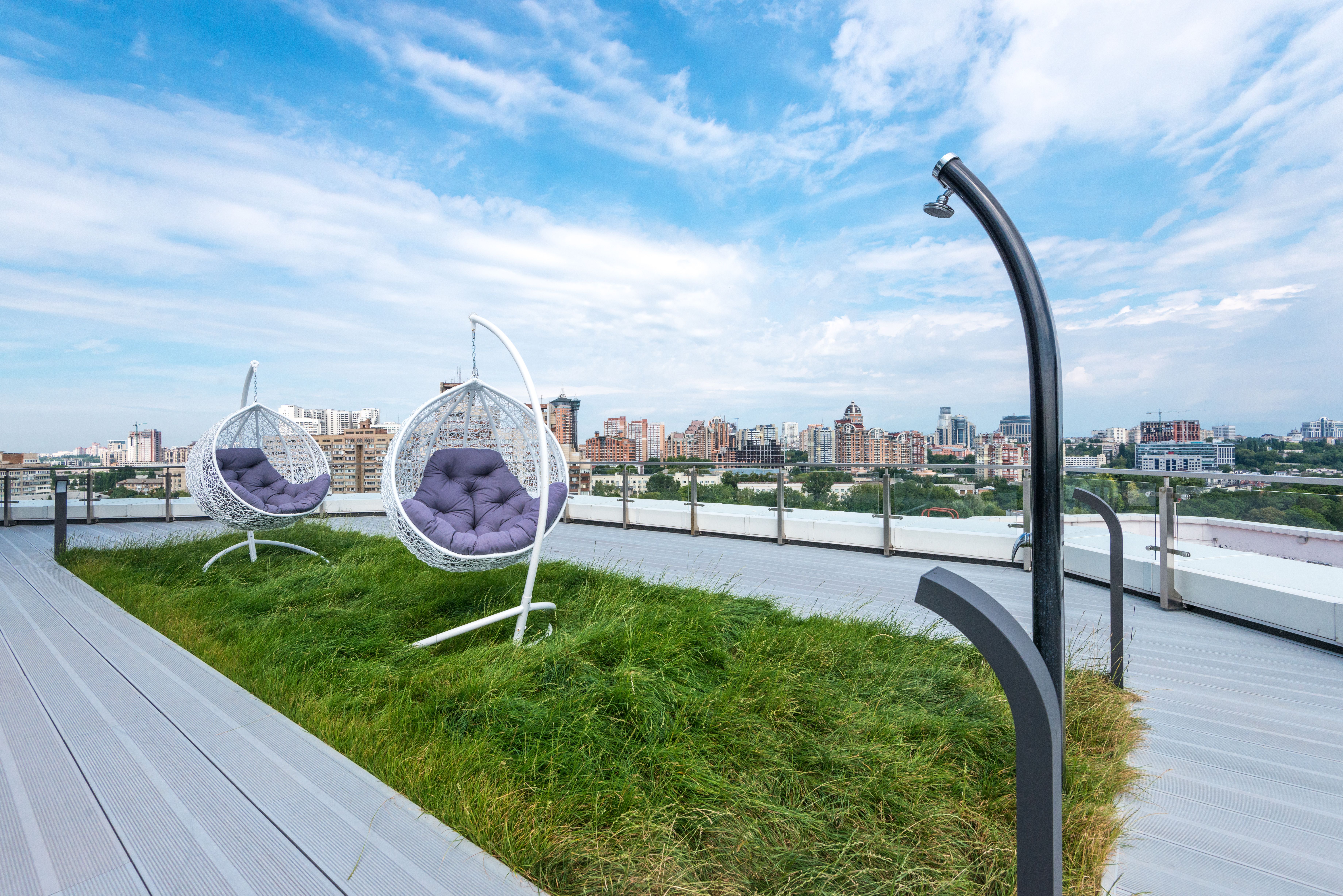 A rooftop terrace with suspended chairs, planted edges, and a city skyline beyond.