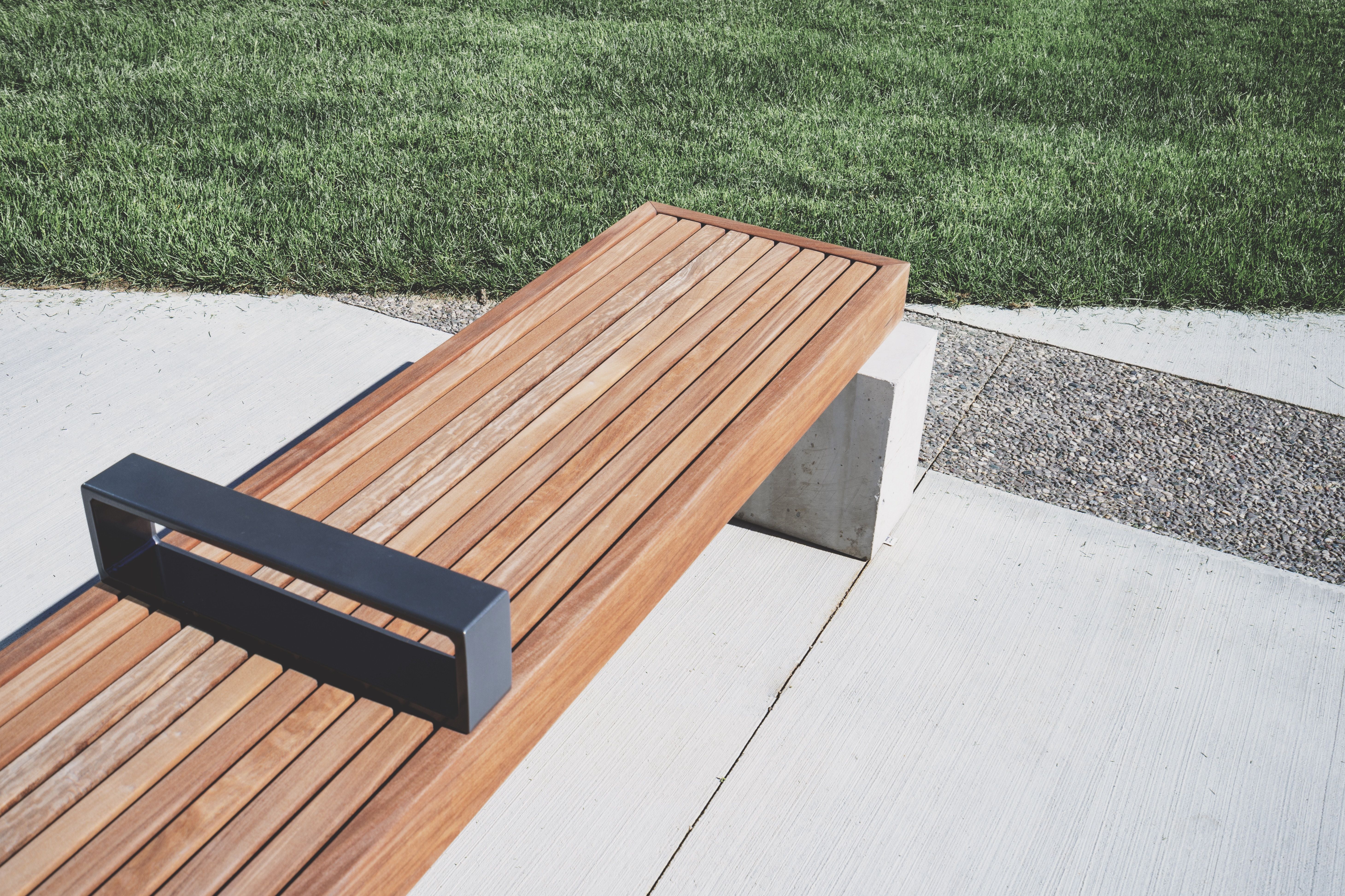 A minimalist timber bench beside a concrete path and green lawn in a contemporary outdoor space.