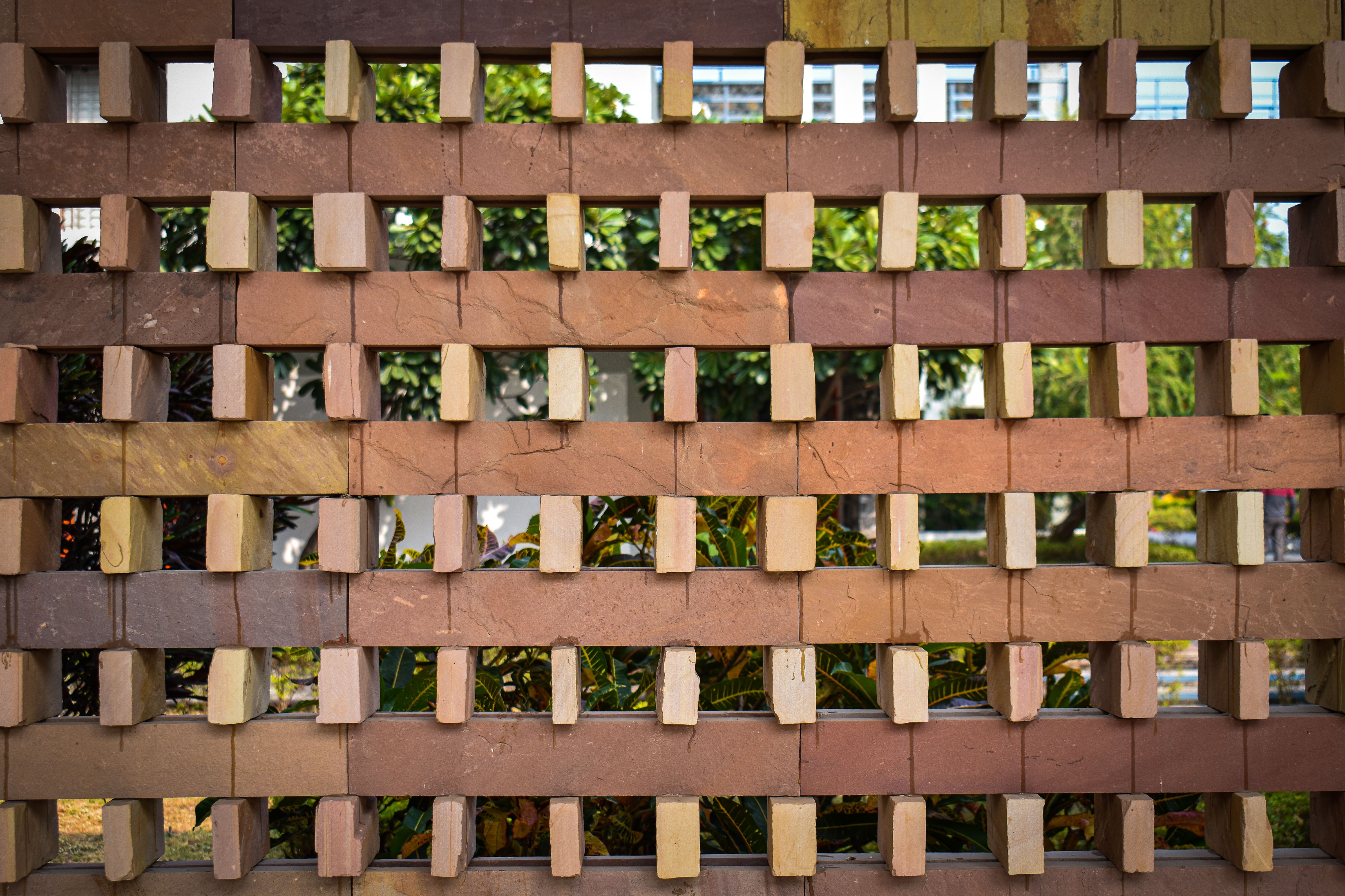 Close view of a patterned openwork brick wall in a sunlit urban park, illustrating a textured, light-filtering landscape material.